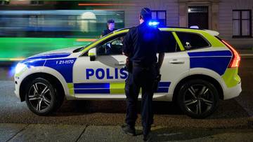 Szwedzki radiow&oacute;z policyjny z włączonymi sygnałami świetlnymi i stojącym obok policjantem.