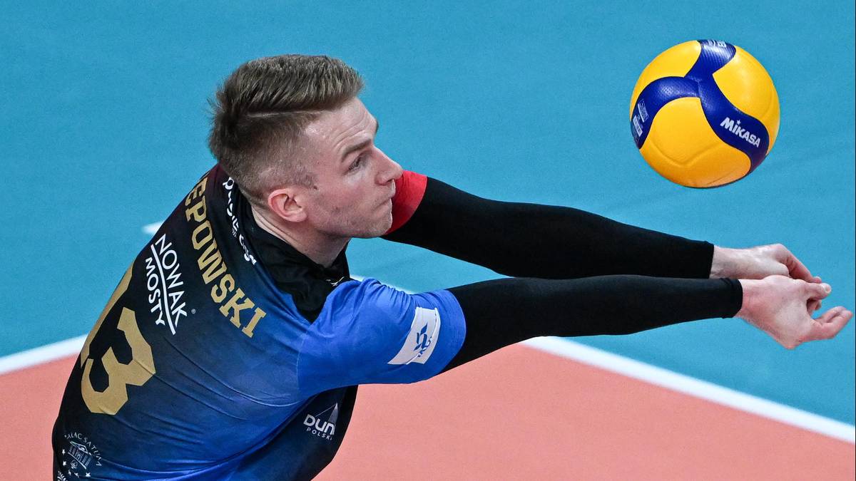 Siatkarz w czarno-niebieskim stroju, z numerem 13 na plecach, odbija piłkę do siatkówki.