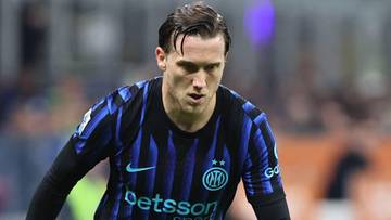 Piłkarz w niebiesko-czarnej koszulce z numerem na plecach prowadzi piłkę po murawie stadionu.