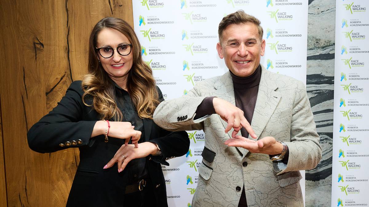 Kobieta i mężczyzna gestykulują rękami na tle logo wydarzenia.