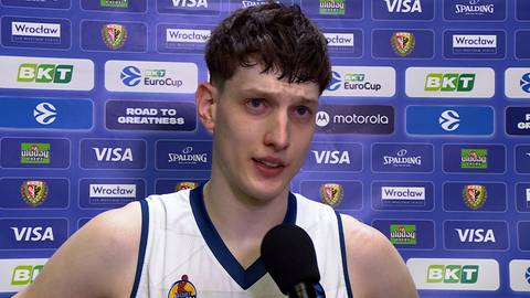 Młody mężczyzna w koszulce sportowej z mikrofonem przed nim.