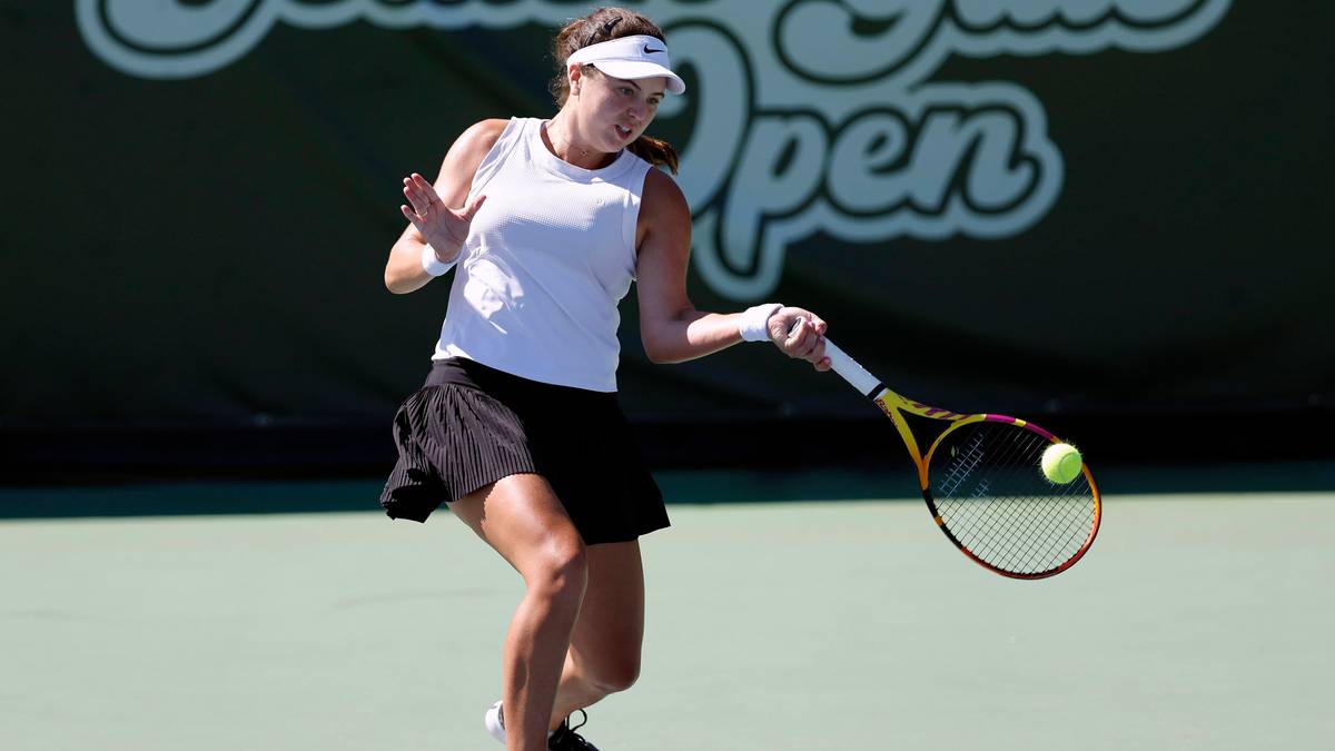 Tenisistka w białej bluzce i czarnej sp&oacute;dnicy uderza piłkę rakietą na korcie tenisowym. W tle logo "Indian Wells Open".