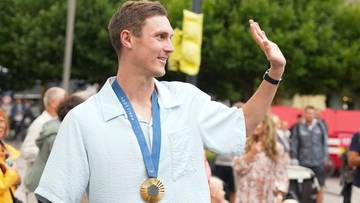 Viktor Axelsen, w jasnej koszuli i z medalem na szyi, macha do zgromadzonych ludzi.