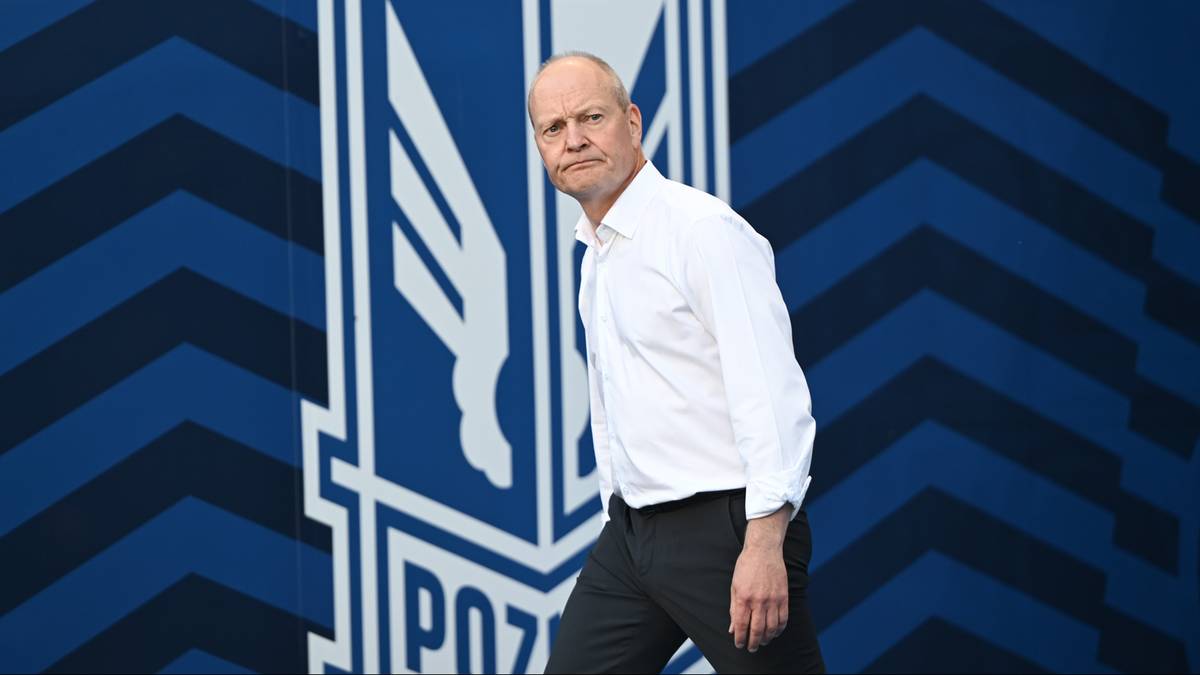 Mężczyzna w białej koszuli przed herbem KKS Lech Poznań.