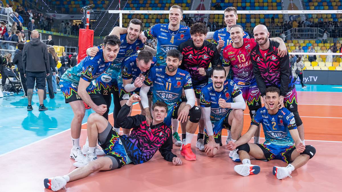 Drużyna siatkarzy pozuje do zdjęcia na boisku sportowym.