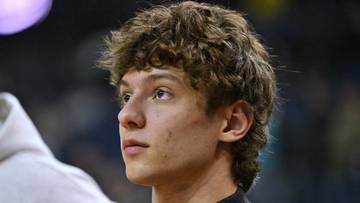 Młody mężczyzna o kręconych włosach patrzy w bok, z profilu.