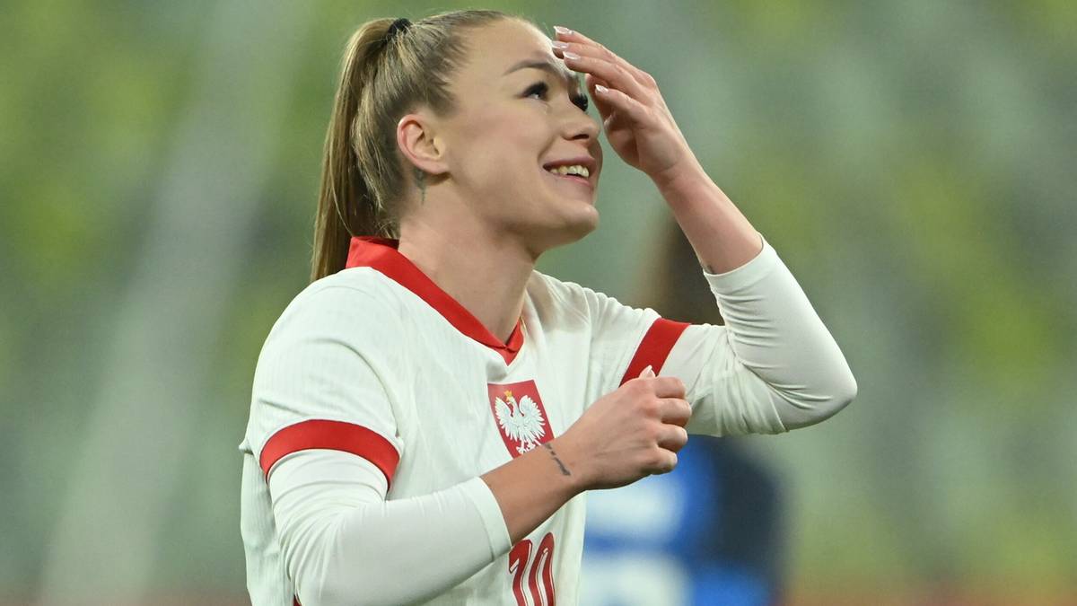 Piłkarka reprezentacji Polski w białej koszulce z czerwonymi detalami, uśmiechnięta, z ręką na czole.