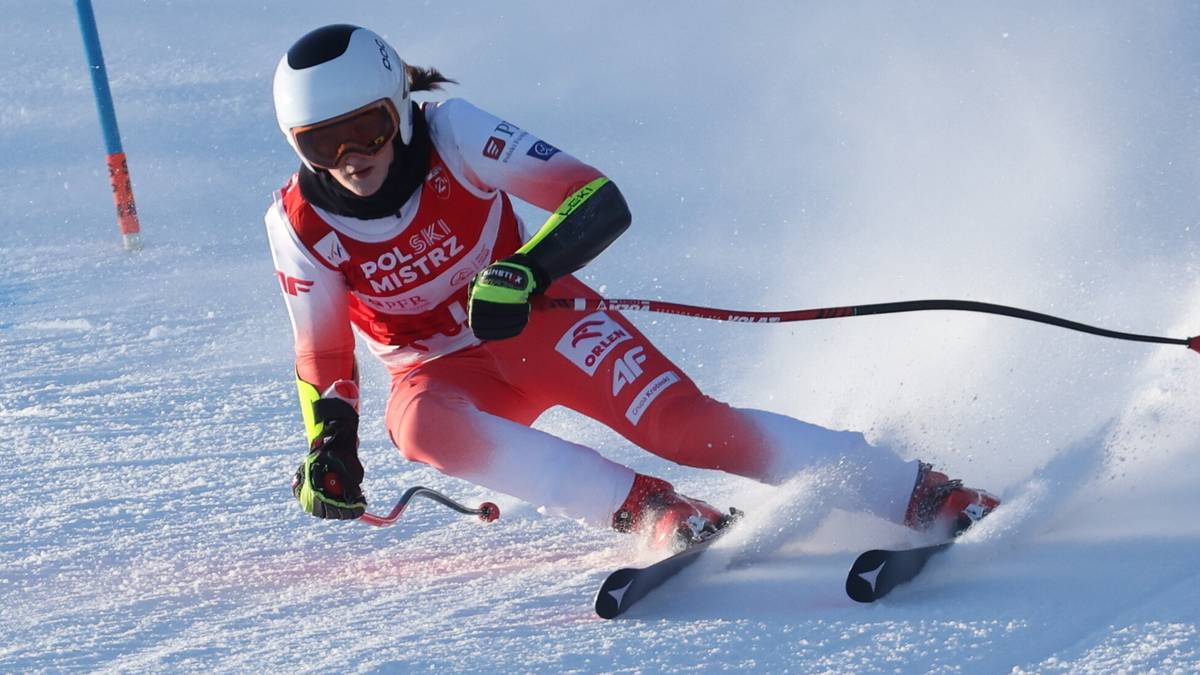 Narciarka alpejska w czerwono-białym stroju zjeżdża po ośnieżonym stoku podczas zawod&oacute;w.