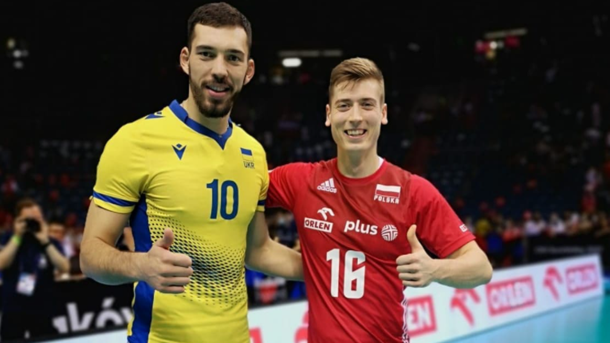 Dw&oacute;ch siatkarzy, jeden w koszulce z numerem 10, drugi z numerem 16, pozuje do zdjęcia uśmiechnięty.