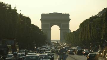 Duży korek samochodowy na ulicy w Paryżu prowadzącej do Łuku Triumfalnego.