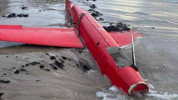 Uszkodzony czerwony dron leżący na plaży przy brzegu morza.