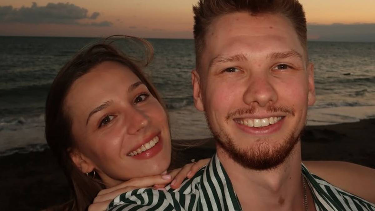 Mężczyzna i kobieta uśmiechają się do kamery na tle zachodzącego słońca i morza.