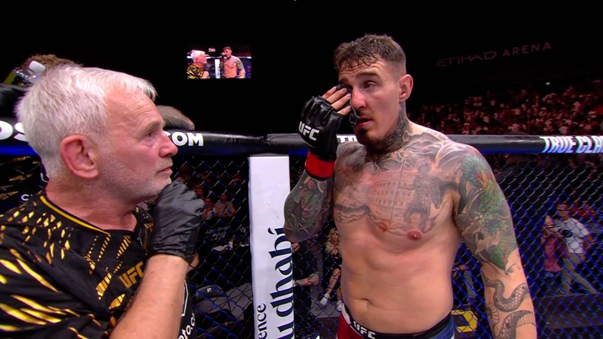 Zawodnik MMA z tatuażami, ocierający łzę z oka, rozmawia z członkiem sztabu UFC w klatce.