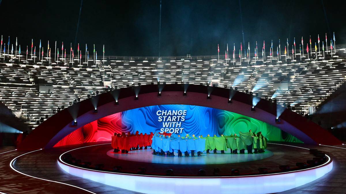 Scena z kolorowym podświetleniem i grupą ludzi pośrodku, na tle trybun stadionu podczas ceremonii otwarcia igrzysk paralimpijskich.