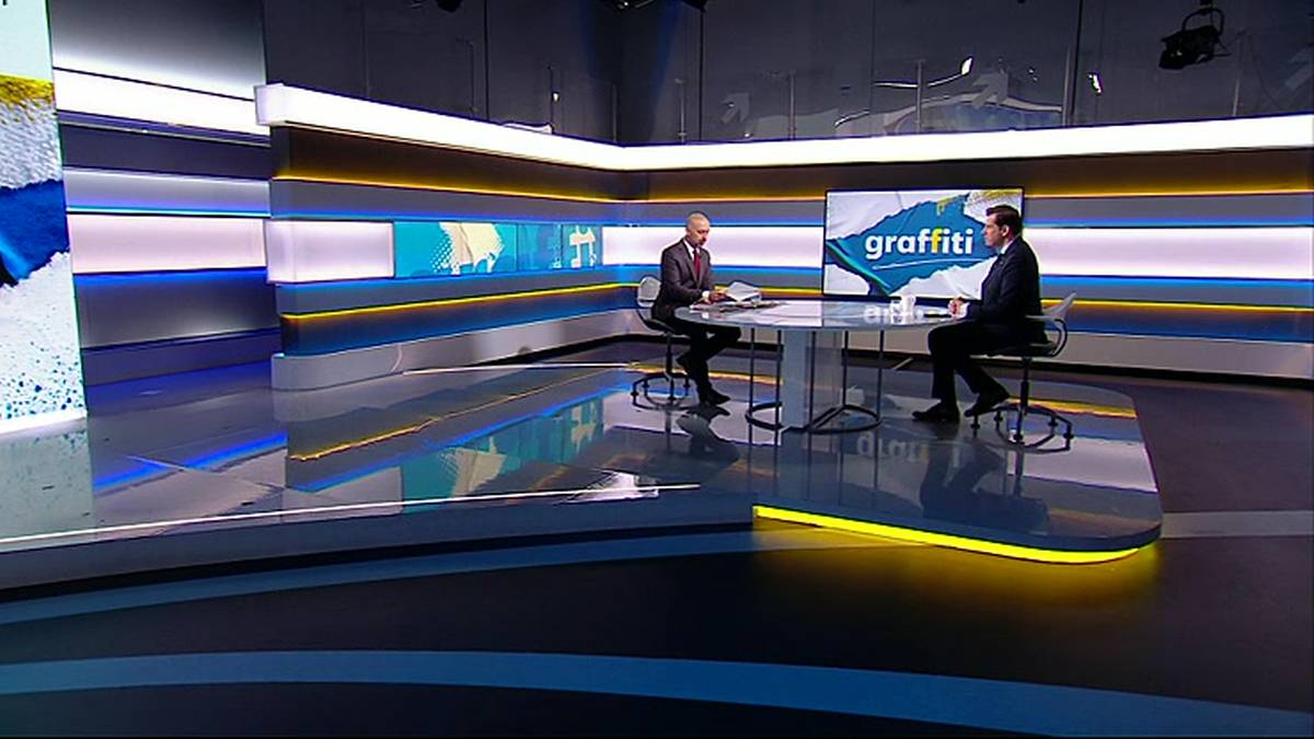 Dw&oacute;ch mężczyzn siedzi przy stole w studiu telewizyjnym z napisem "graffiti" na ekranie.