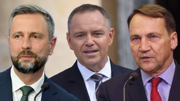 Trzej mężczyźni w garniturach stojący przed mikrofonami.