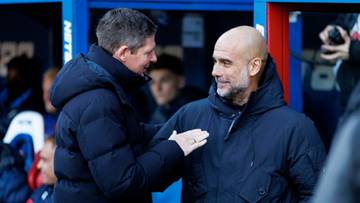 Dw&oacute;ch mężczyzn w ciemnych kurtkach rozmawia, jeden z nich klepie drugiego po ramieniu.