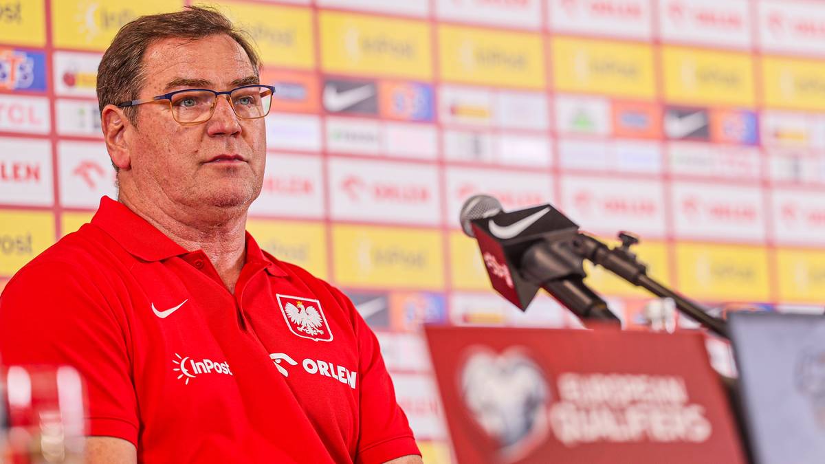 Jerzy Brzęczek, trener reprezentacji Polski w piłce nożnej, w czerwonej koszulce z logo polskiej federacji, przed mikrofonami.