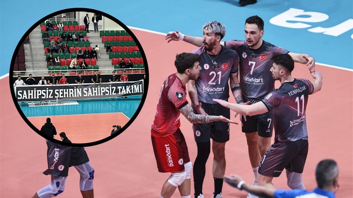 Siatkarze w czerwonych strojach stoją razem, z lewej strony widoczne koło z transparentem "SAHİPSİZ ŞEHİR SAHİPSİZ TAKIM" na tle trybun.