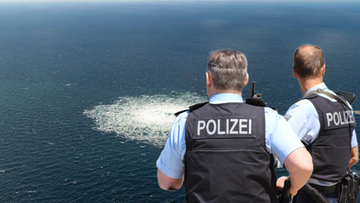 Dwóch policjantów w mundurach z napisem "POLIZEI" obserwuje na morzu spienioną wodę, wskazującą na wyciek z gazociągu.