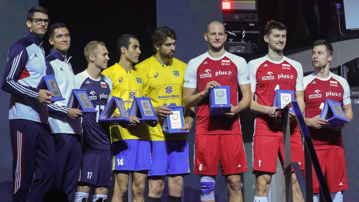 Grupa męskich siatkarzy w strojach sportowych, kilku z nich trzyma medale i puchary na podium.