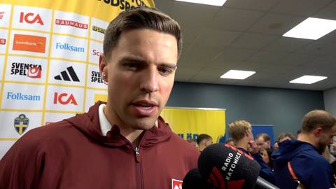 Jan Bednarek, polski piłkarz, podczas udzielania wywiadu. Ma na sobie bordową bluzę. W tle widoczne są logotypy sponsor&oacute;w i inne osoby.