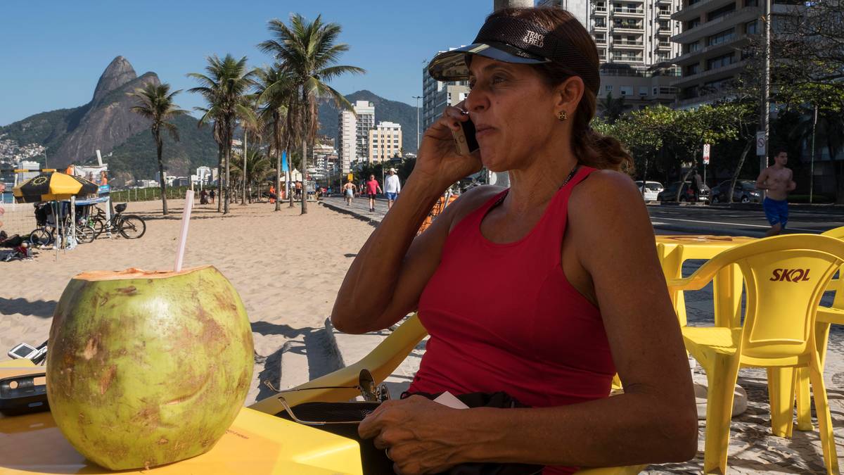 Kobieta rozmawia przez telefon na plaży, obok kokos z napojem.