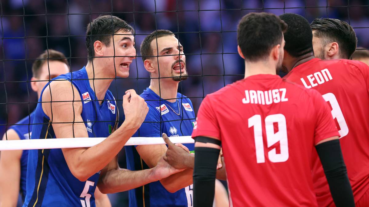 Siatkarze w niebieskich strojach rozmawiają przy siatce z zawodnikami w czerwonych koszulkach.