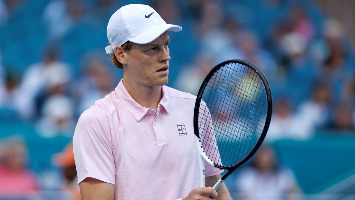 Jannik Sinner trzyma rakietę tenisową podczas meczu, ubrany w różową koszulkę i białą czapkę.