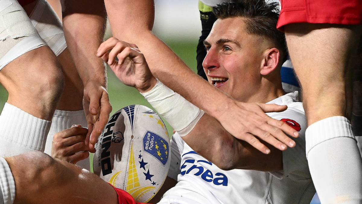 Rugbista w białej koszulce cieszy się po zdobyciu punkt&oacute;w, otoczony przez innych graczy.