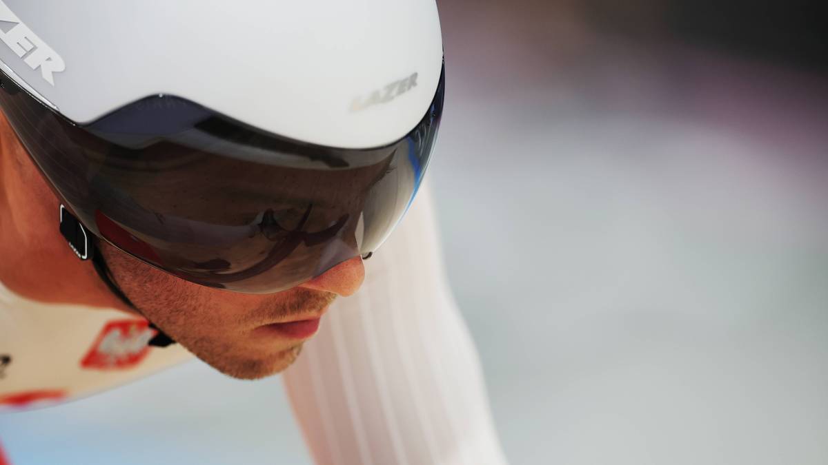 Kolarz w białym kasku z ciemną szybką, widoczny profil twarzy z zarostem, na kasku widoczne logo "LAZER".