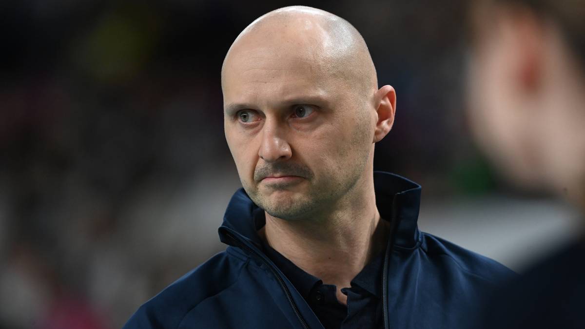 Portret łysiejącego mężczyzny w środku rozmowy, patrzącego w bok z poważną miną, w ciemnej kurtce sportowej.