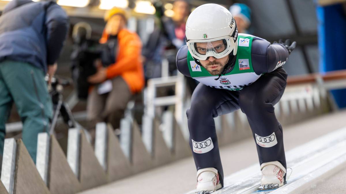 Skoczek narciarski w pozycji startowej na desce rozbiegu.