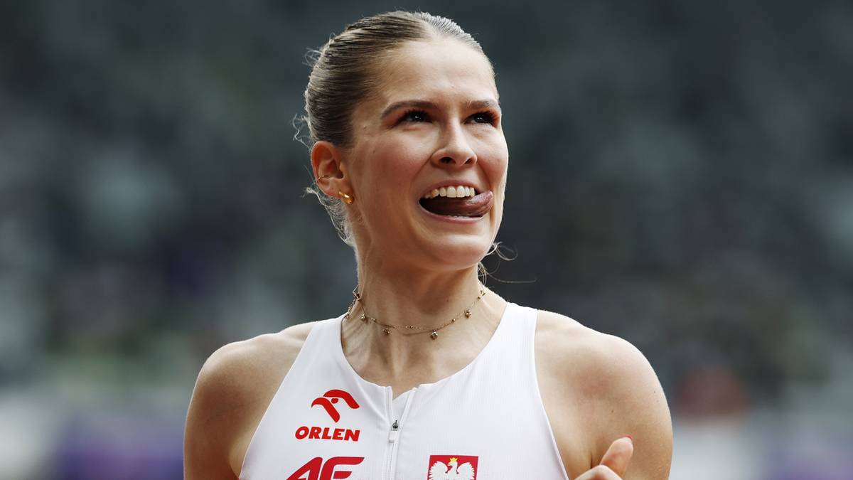 Portret lekkoatletki w białej koszulce z godłem Polski, uśmiechniętej, w trakcie zawodów.