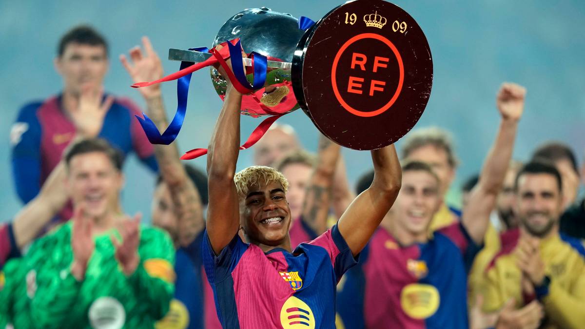 Lamine Yamal trzyma trofeum, z uśmiechem na twarzy, w otoczeniu innych piłkarzy.