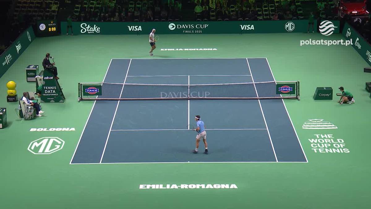 Dwaj zawodnicy tenisa na korcie ziemnym podczas meczu, z siatką pośrodku i trybunami w tle.