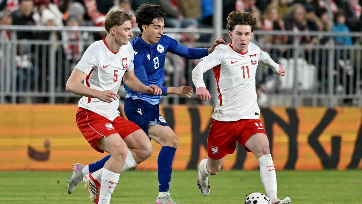 Trzech młodych piłkarzy podczas meczu, dw&oacute;ch w białych strojach z orłem, jeden w niebieskim.