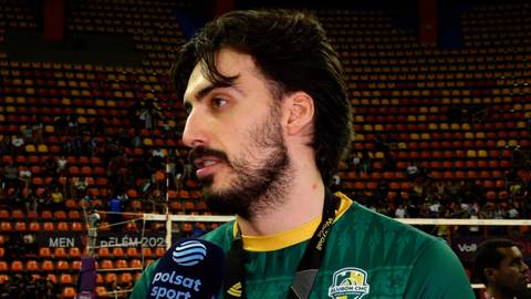 Mężczyzna z brodą i ciemnymi włosami, ubrany w zieloną koszulkę sportową, trzyma mikrofon Polsat Sport i m&oacute;wi do kamery. W tle widać trybuny pełne widz&oacute;w.