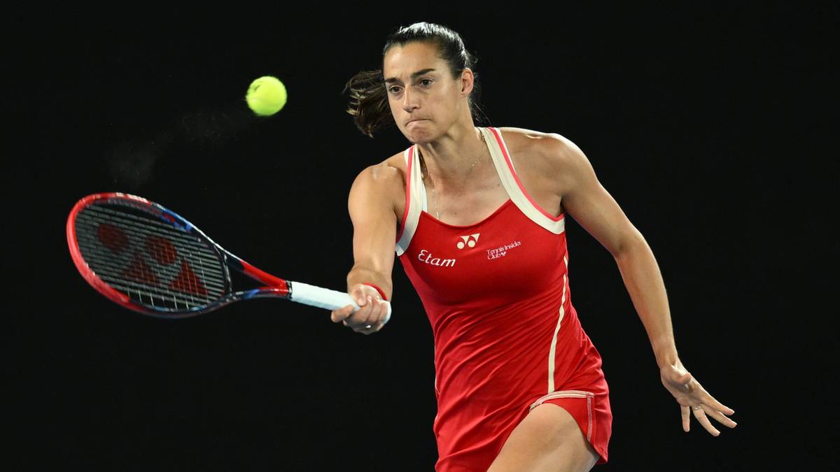 Kobieta w czerwonym stroju tenisowym uderza rakietą piłkę do tenisa na czarnym tle.