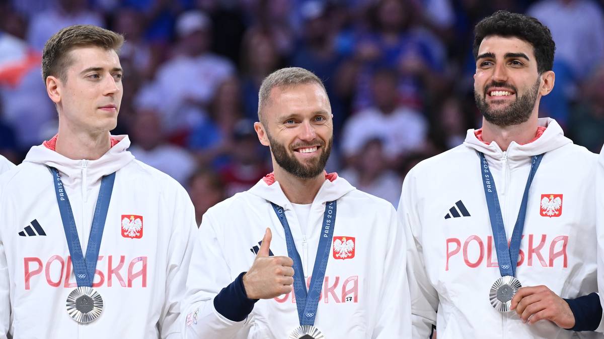 Trzech siatkarzy z medalami na szyi, stojących obok siebie, patrzących w kierunku widza. W środku jeden z nich uśmiecha się i daje kciuk w górę.