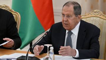 Siergiej Ławrow, minister spraw zagranicznych Rosji, siedzi przy stole podczas konferencji prasowej, przemawiając z gestykulacją. W tle widoczna jest flaga Białorusi.