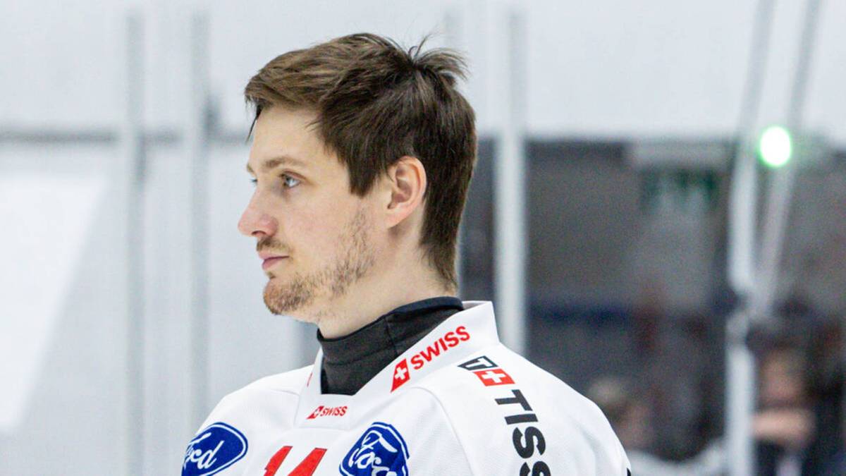 Trzech hokeistów w białych strojach z czerwonymi krzyżami na piersi stoi obok siebie na lodowisku.