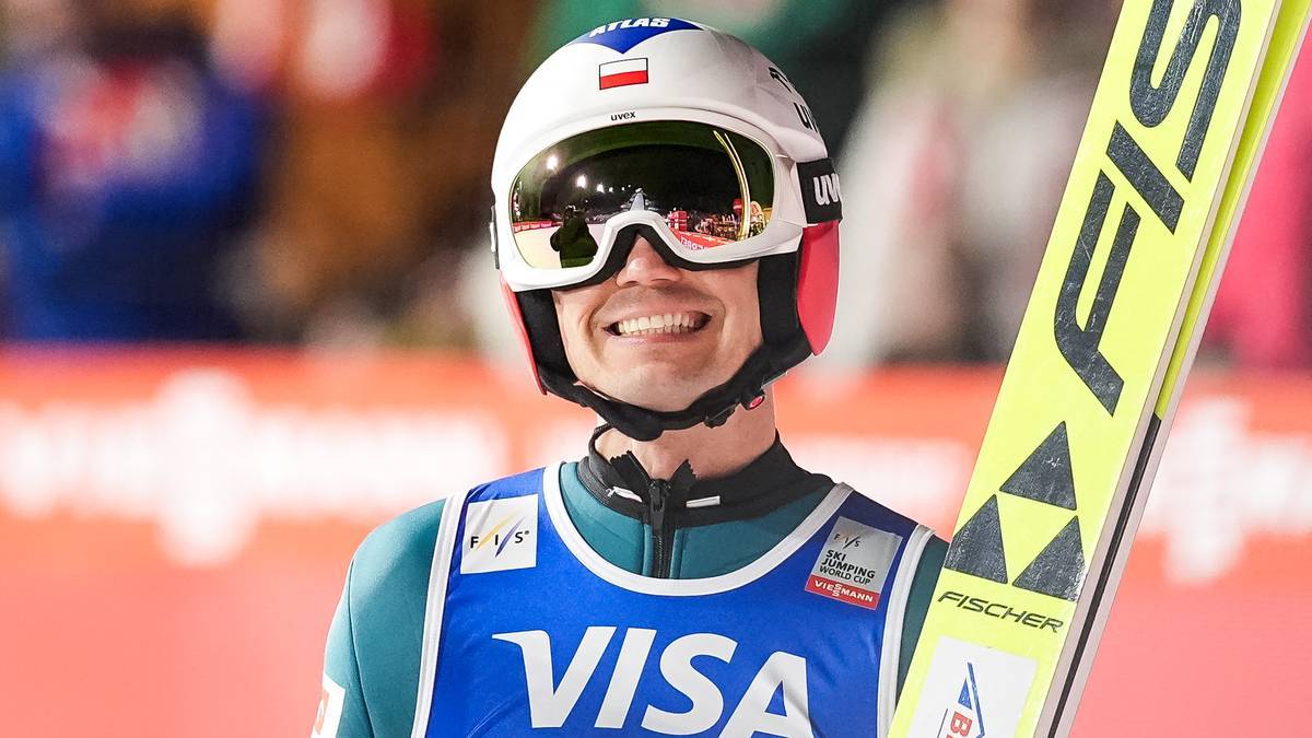 Skoczek narciarski w kasku i goglach, trzymający nartę.