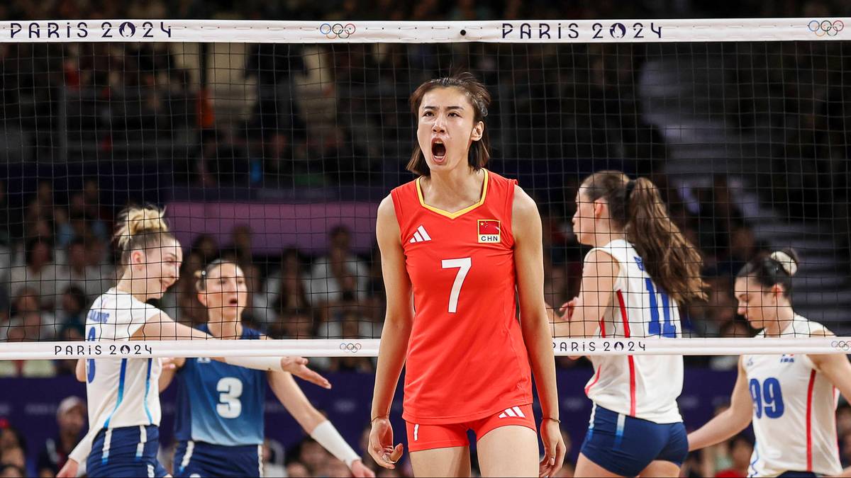 Siatkarka w czerwonej koszulce z numerem 7 krzyczy podczas meczu siatkówki, inne zawodniczki w tle.