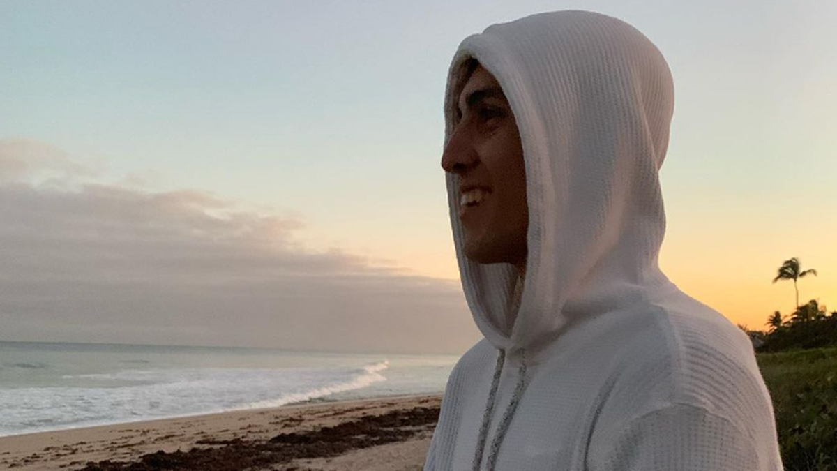 Portret młodego mężczyzny w białej bluzie z kapturem na plaży o zachodzie słońca.