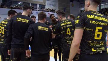 Grupa siatkarzy w czarnych strojach z ż&oacute;łtymi napisami stoi w k&oacute;łku podczas odprawy taktycznej.