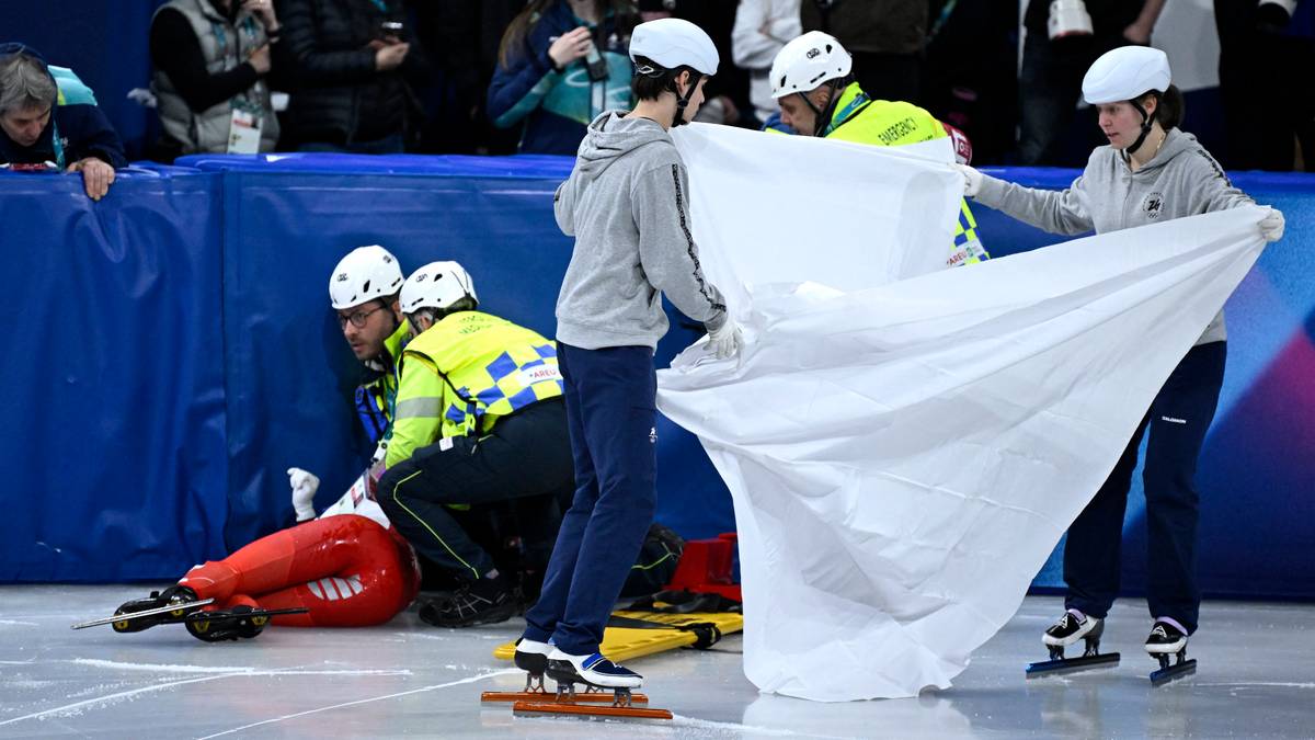 Zawodniczka leżąca na lodowisku, otoczona przez ratownik&oacute;w medycznych i innych łyżwiarzy, zasłonięta białym materiałem.