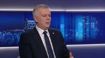 Tomasz Siemoniak, ubrany w ciemny garnitur i krawat, siedzi i mówi, na tle ekranów z nocnym widokiem miasta.