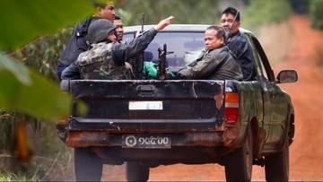 Grupa uzbrojonych żołnierzy w mundurach siedzi na pace czarnego pickupa, jeden z nich wskazuje ręką przed siebie.