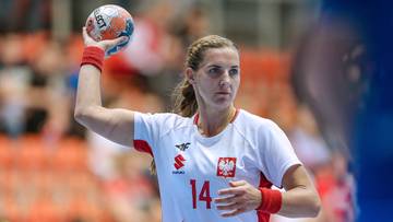 Piłkarka ręczna w białej koszulce z czerwonymi elementami, z numerem 14, podnosi piłkę do rzutu.